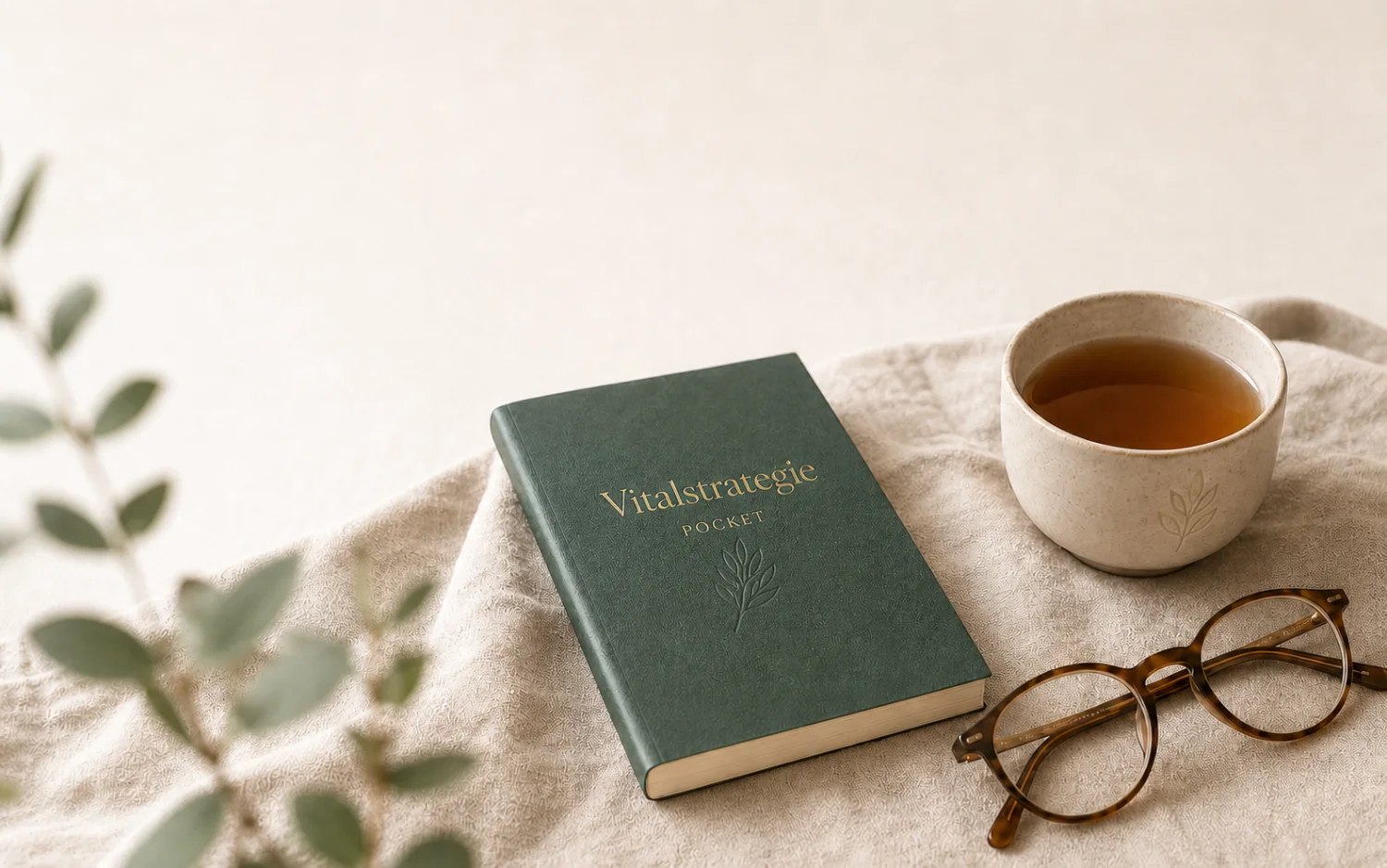 Grünes Pocket-Book, eine Tasse Tee und eine Lesebrille auf hellem Leinen